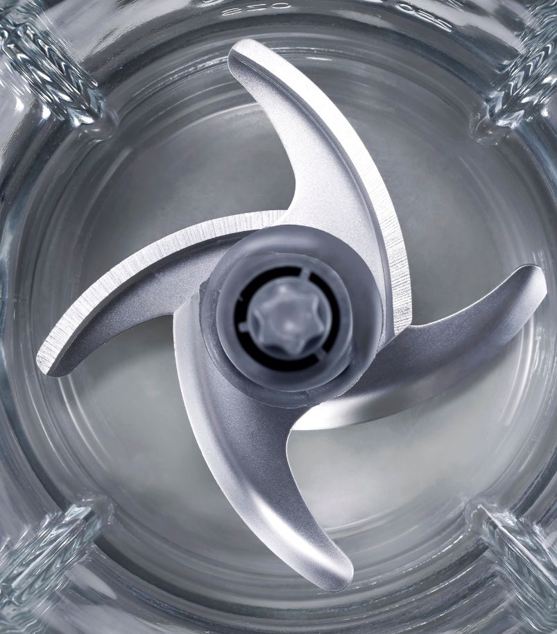 Imagem em close-up das lâminas de um liquidificador de quatro pontas em metal, vistas de cima dentro de um copo de vidro. A imagem foca na manutenção e limpeza das lâminas para garantir a eficiência do aparelho.