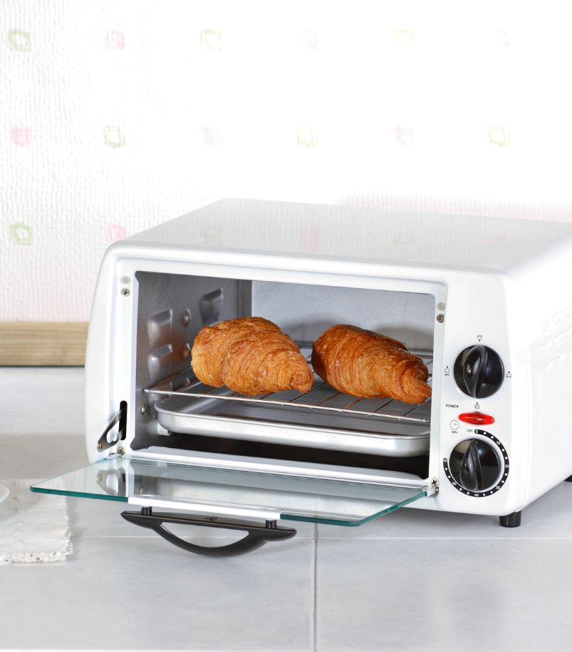 Forno elétrico de bancada, na cor branca, com a porta de vidro entreaberta, mostrando dois croissants perfeitamente dourados e assados na bandeja interna.