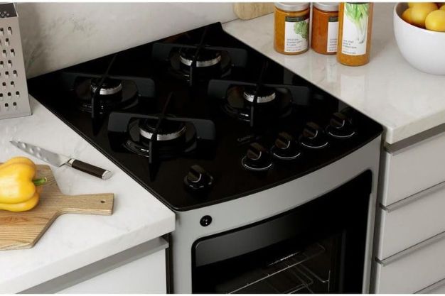 Vista superior de um fogão 4 bocas com mesa de vidro preta em uma cozinha moderna com bancada branca.