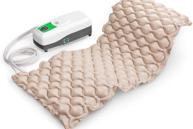 Colchão pneumático com compressor ao lado, ilustrando o que é colchão pneumático e como o sistema de câmaras de ar funciona para prevenir lesões por pressão.