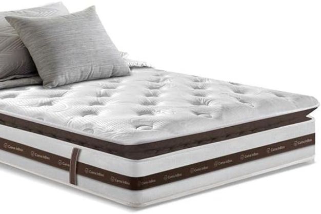 Colchão branco moderno com Pillow Top (camada extra de conforto) visível na parte superior, destacando o que é pillow top no colchão para um sono mais macio. Três travesseiros cinza estão na cabeceira.