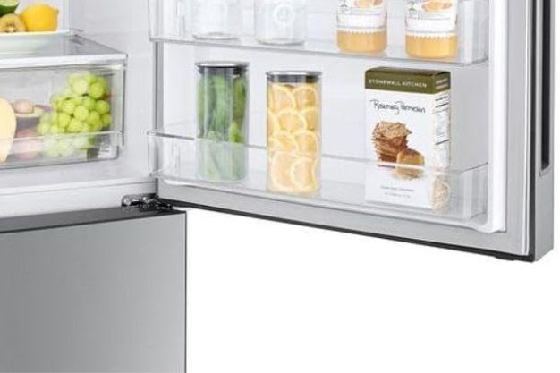 Interior de geladeira com porta aberta, prateleiras organizadas com bebidas, frutas e alimentos embalados