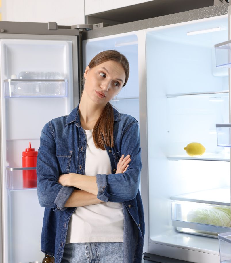 frigobar-ou-geladeira Mulher diante de geladeira aberta quase vazia em comparação entre frigobar ou geladeira