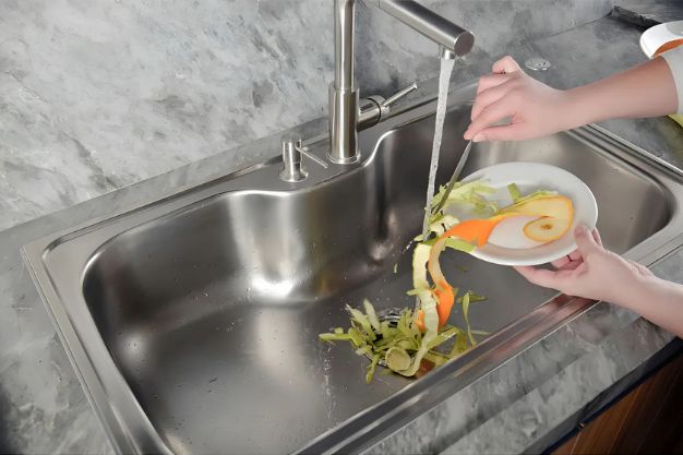Pessoa descartando restos de alimentos na pia para triturador de alimentos