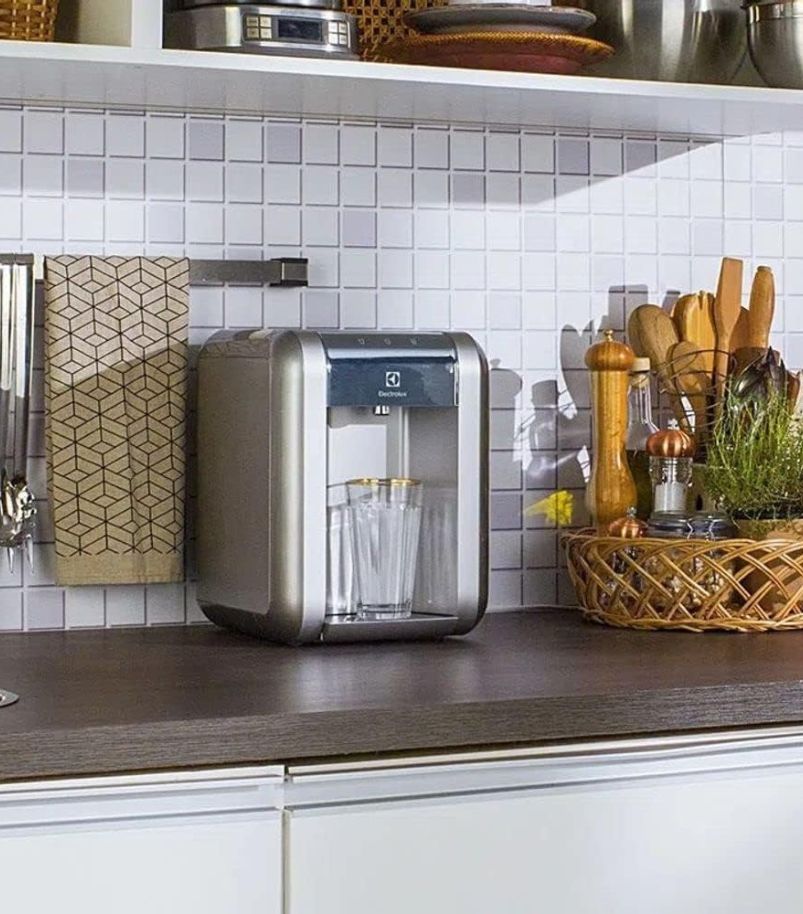 Purificador de água instalado sobre bancada de cozinha com copos posicionados abaixo