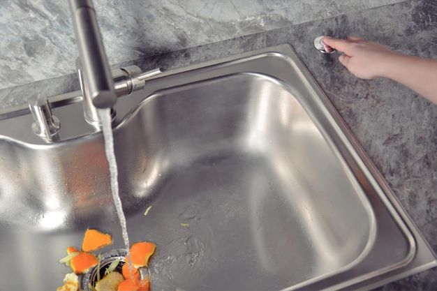 Pessoa acionando botão do triturador de alimentos ao lado da pia