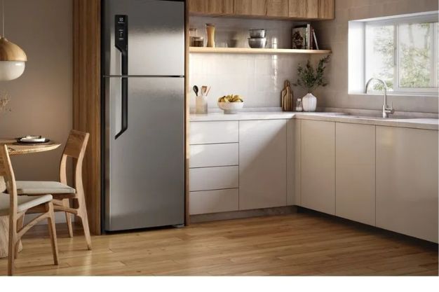 Geladeira duplex inox instalada em cozinha moderna planejada com armários claros e mesa de madeira