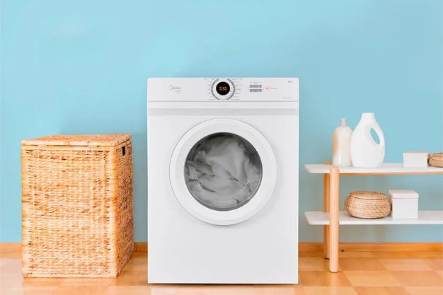 Secadora de roupas branca em lavanderia com cesto de roupas e prateleira com produtos de limpeza