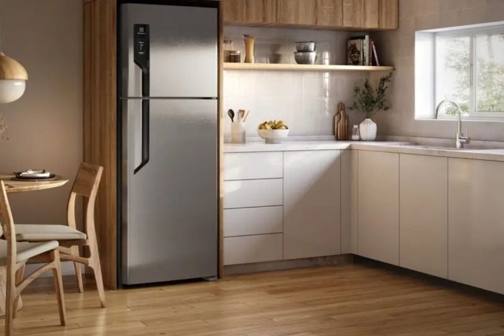 Geladeira duplex inox posicionada em cozinha moderna com armários claros e acabamento amadeirado