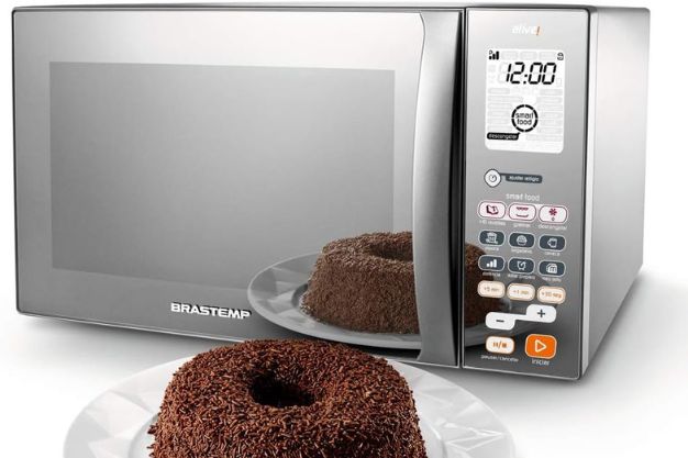 Micro-ondas Brastemp com painel digital ao lado de bolo de chocolate servido em prato sobre bancada