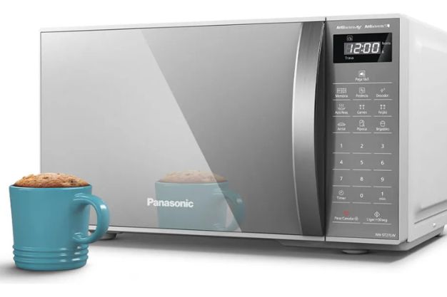 Micro-ondas Panasonic com painel digital ao lado de caneca com bolo sobre superfície branca